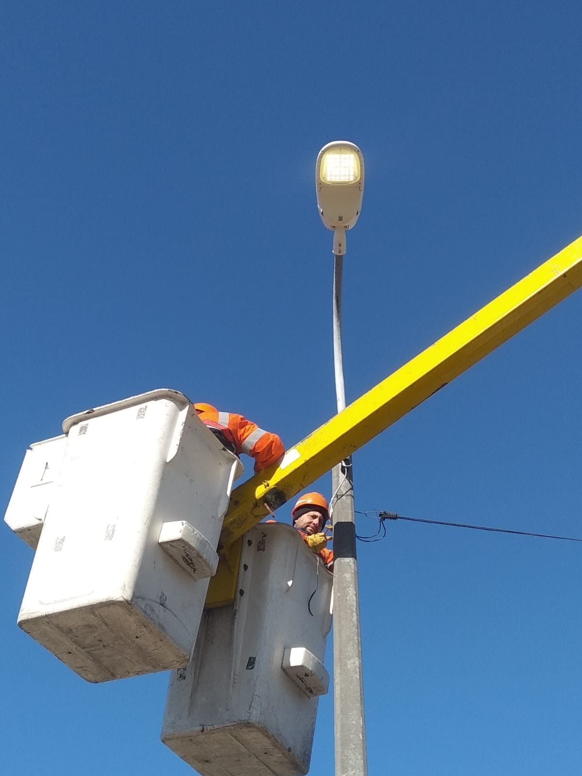 Aerial-platform installation crew beside an LED road luminaire in the municipality